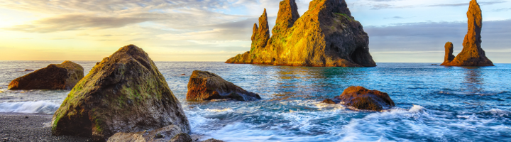 Rotsformaties bij Reynisfjara Beach in IJsland, met golven en avondlicht.