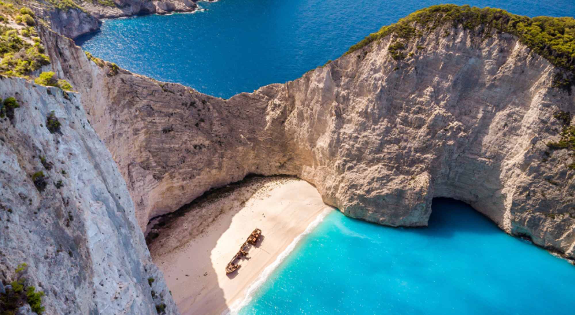 Uitzicht op Navagio Beach op Zakynthos met scheepswrak op wit zand en helderblauwe zee, omringd door kliffen.
