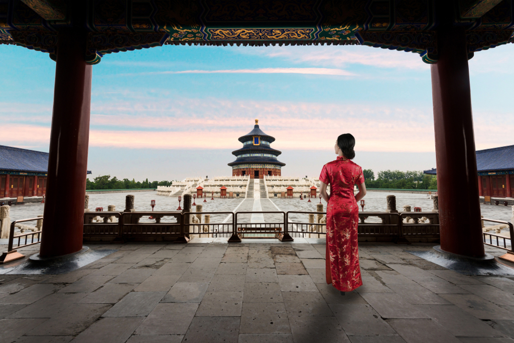 Vrouw in rode qipao kijkt uit op de Tempel van de Hemel in Beijing tijdens een groepsrondreis China.