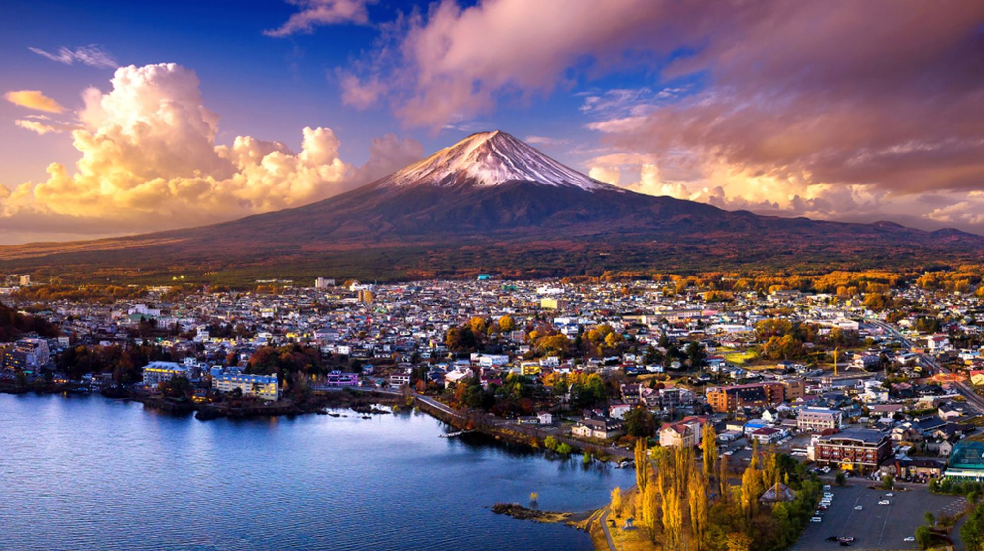 Uitzicht op de besneeuwde Mount Fuji boven Kawaguchiko, met het meer en de stad in de voorgrond bij zonsondergang.