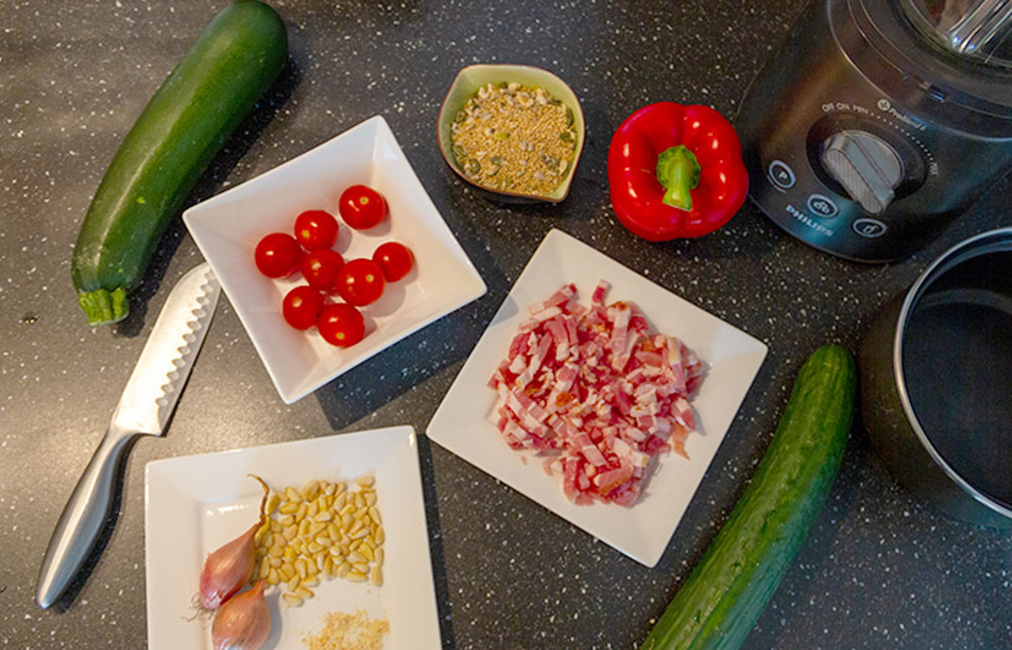 Ingrediënten voor een courgetterecept: courgette, cherrytomaten, paprika, spekreepjes, knoflook en pitten.
