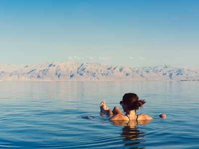 Reiziger drijft ontspannen in de Dode Zee in Jordanië, met bergen op de achtergrond.