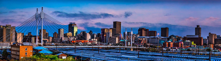 Skyline van Johannesburg met Nelson Mandela Bridge en spoorlijnen bij zonsondergang.