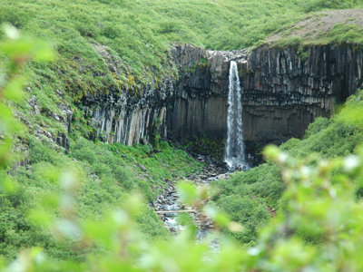 Waterval in groene kloof met basaltrotsen langs de route van een groepsrondreis IJsland kamperen.