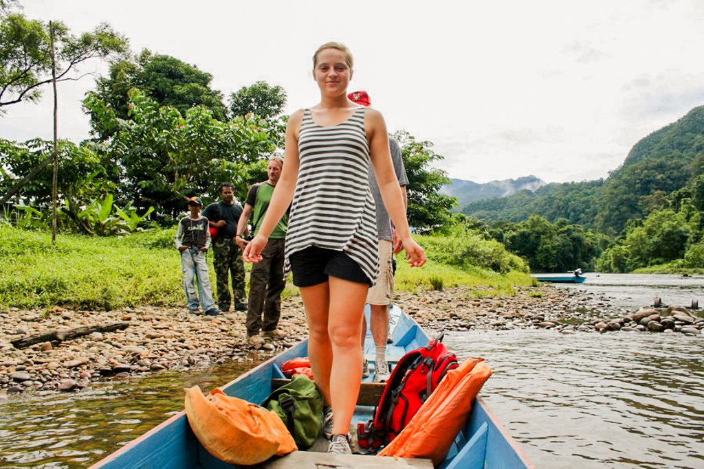Jongere op een longboat op de rivier in Maleisisch Borneo tijdens een familiereis, met jungle en bergen op de achtergrond.