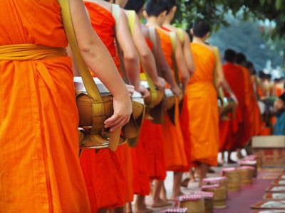 Monniken in oranje gewaden in een rij tijdens de ochtendronde met offergaven in Laos & Cambodja-route.