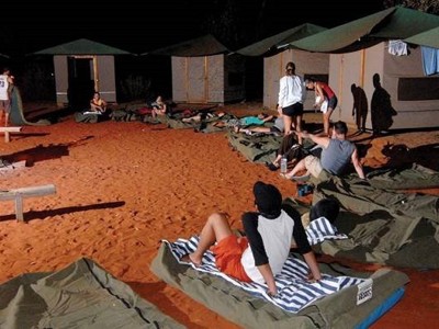 Kamperen in Australië: reizigers liggen op swags rond het kampvuur in de rode woestijn bij tenten.