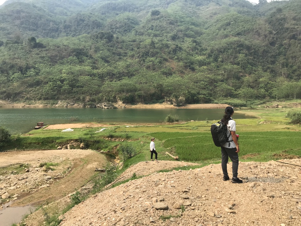Backpackers wandelen langs rijstvelden en een rivier in de groene bergen van Vietnam tijdens een 22-35ers reis.