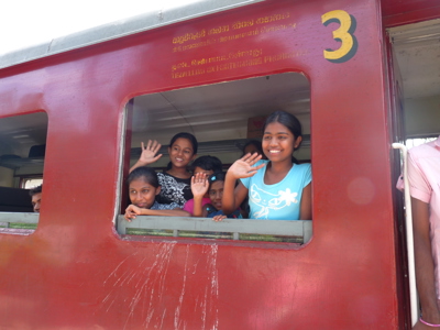 Vrolijke kinderen zwaaien vanuit een rode trein in Sri Lanka, onderdeel van de Route Sri Lanka.