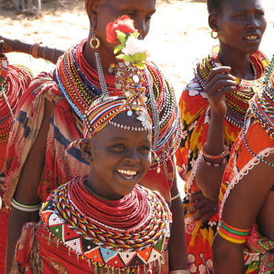 Vrolijk meisje en vrouwen in kleurrijke Masai-kleding en kralensieraden tijdens familiereis in Kenia, Tanzania en Zanzibar.