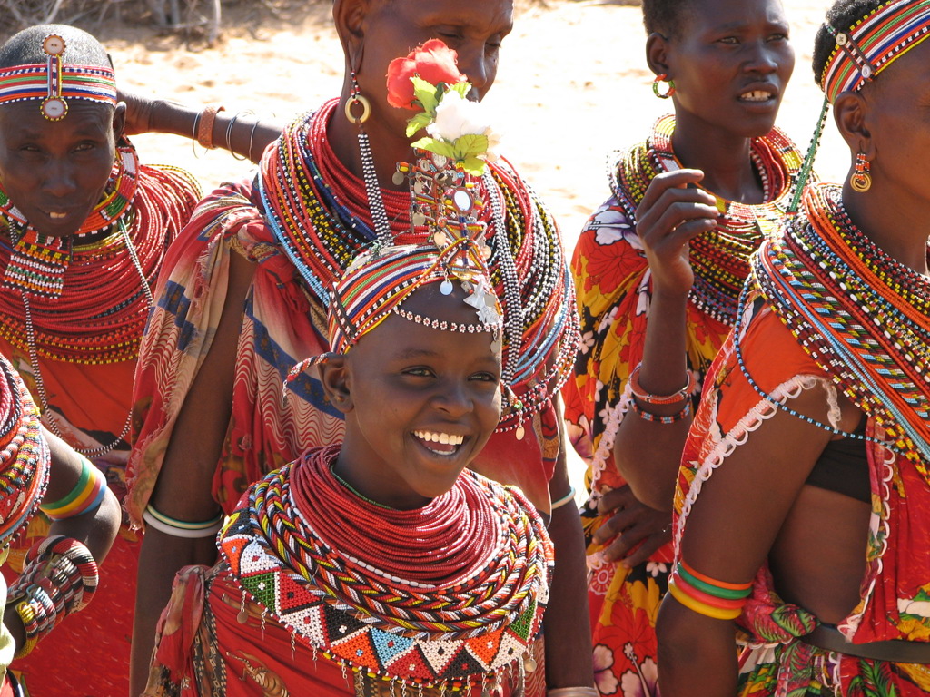 Vrolijk meisje en vrouwen in kleurrijke Masai-kleding en kralensieraden tijdens familiereis in Kenia, Tanzania en Zanzibar.