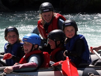 Gezin tijdens wildwaterraften in de Écrins, Frankrijk, met helmen en zwemvesten op een snelstromende rivier.