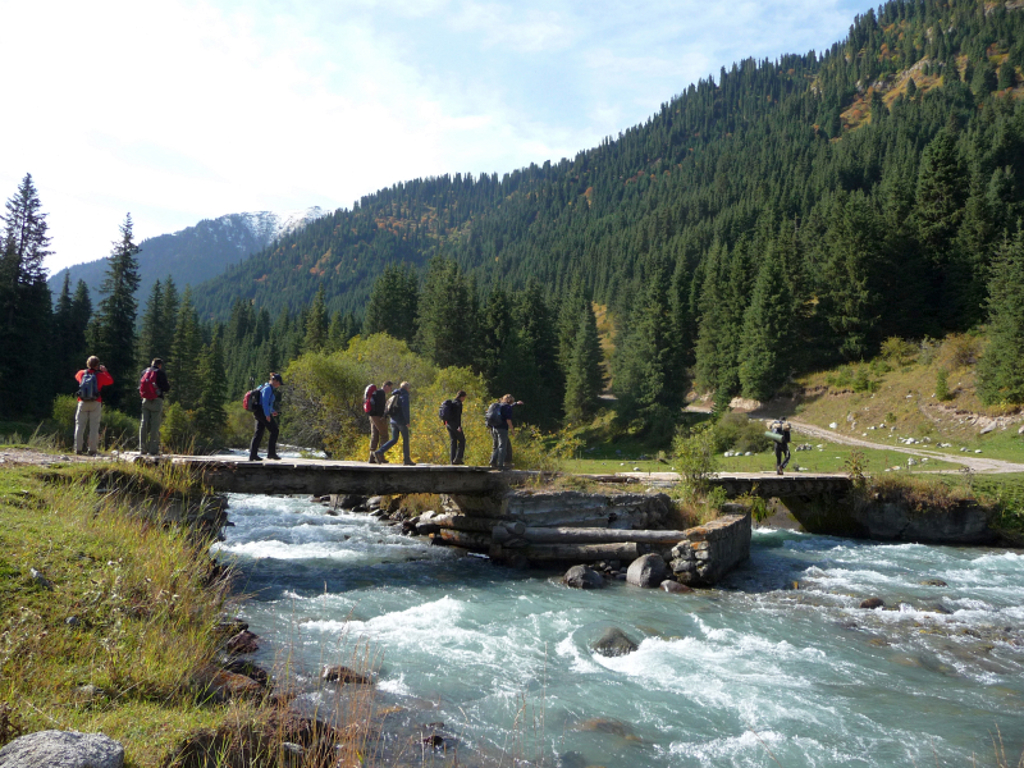 Wandelaars steken een brug over een bergbeek over tijdens groepsrondreis Kirgistan (Kirgizië) langs de Zijderoute.