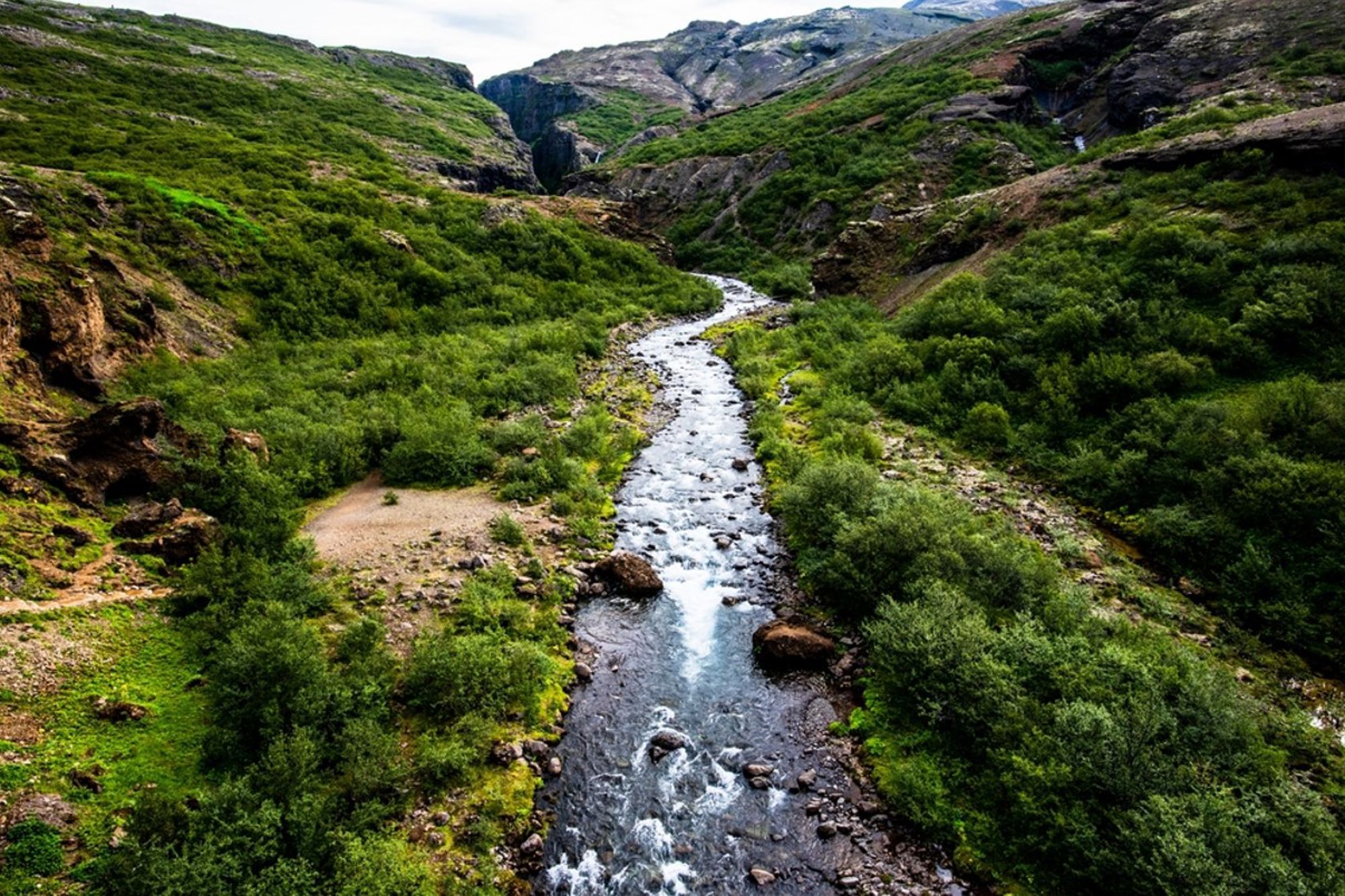 Rivier in een groene vallei tussen rotsachtige bergen in IJsland.