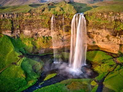 Seljalandsfoss-waterval in Zuid-IJsland, met groene kliffen en wandelpad achter de waterval.