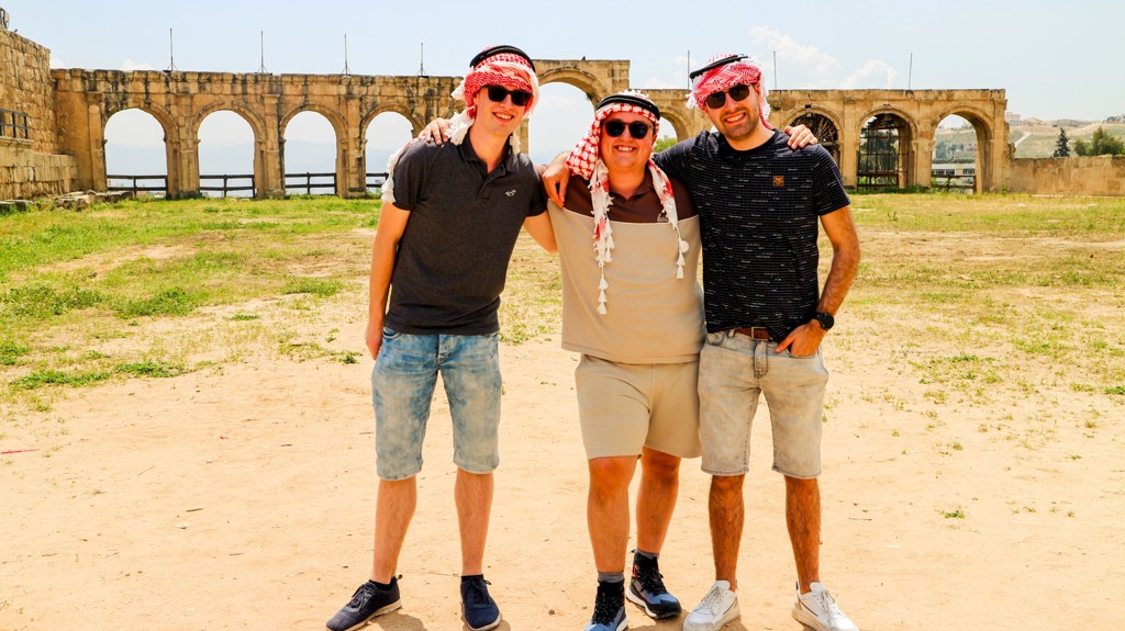 Drie vrienden met keffiyeh poseren bij oude Romeinse bogen tijdens een 22-35ers reis in Jordanië.