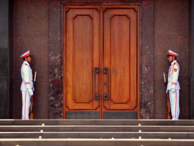 Erewachten in wit uniform bij een grote houten deur in Hanoi, Vietnam.