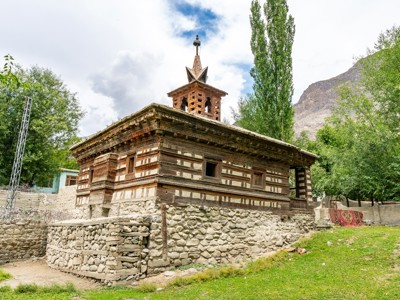 Traditionele houten moskee in de Hunza-vallei, Pakistan, met stenen fundament en bergen op de achtergrond.