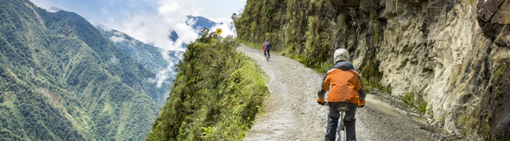 Fietsers op de Death Road langs een steile bergwand met uitzicht op groene valleien in Bolivia.