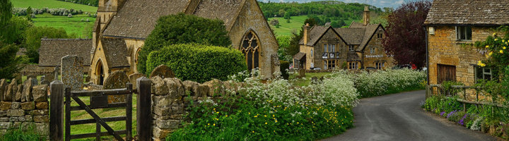 Cotswolds-dorp met stenen cottages en kerk langs een landelijke weg in het Verenigd Koninkrijk.