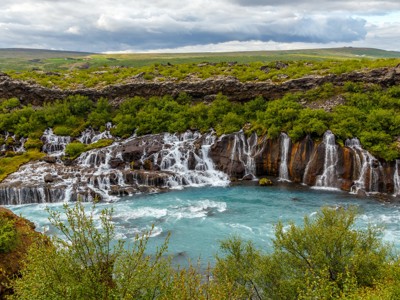 Waterval met turquoise rivier in groen lavalandschap langs de Route IJsland.