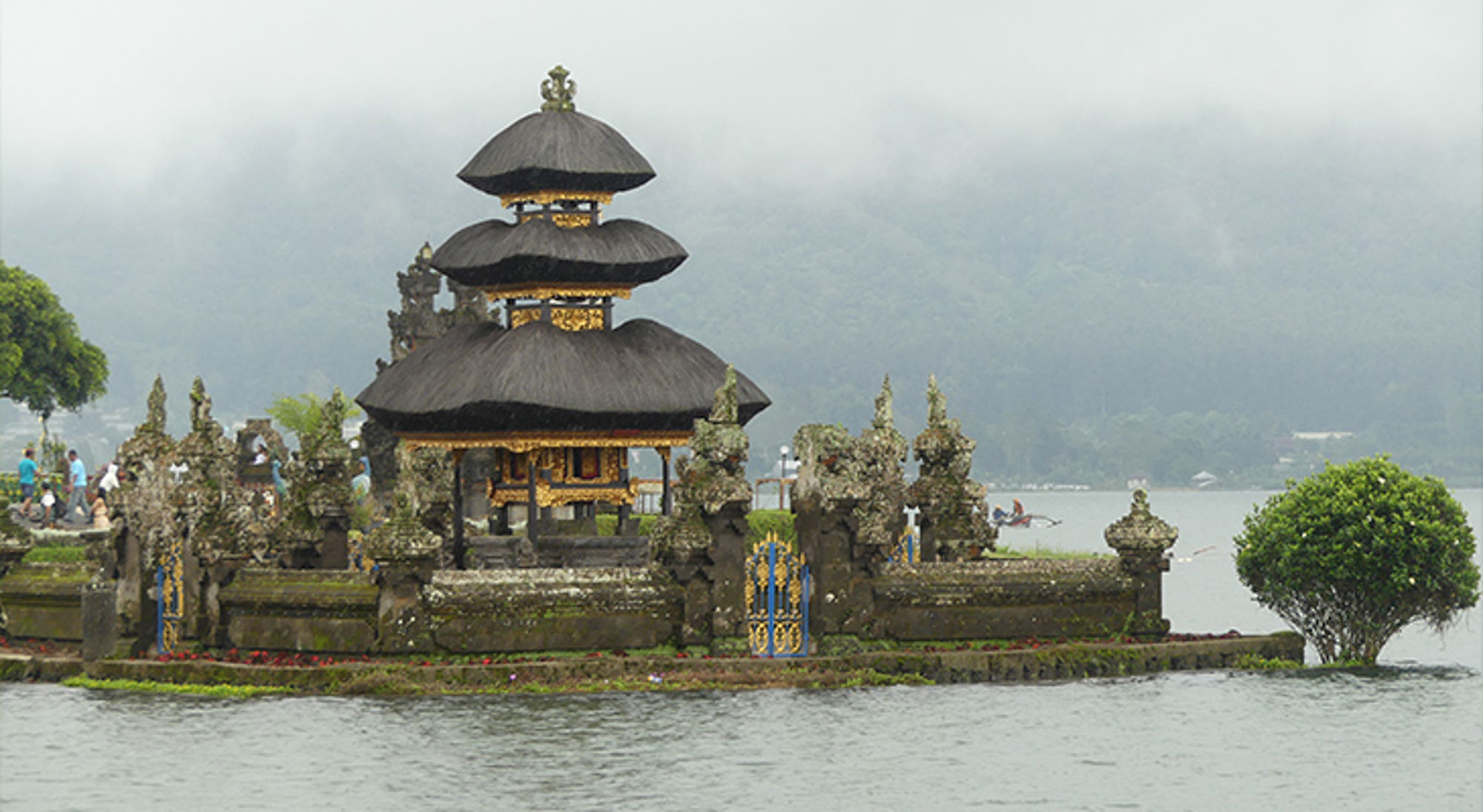 Hindoeïstische tempel met meerlaagse pagodedaken aan het water, met bergen op de achtergrond.