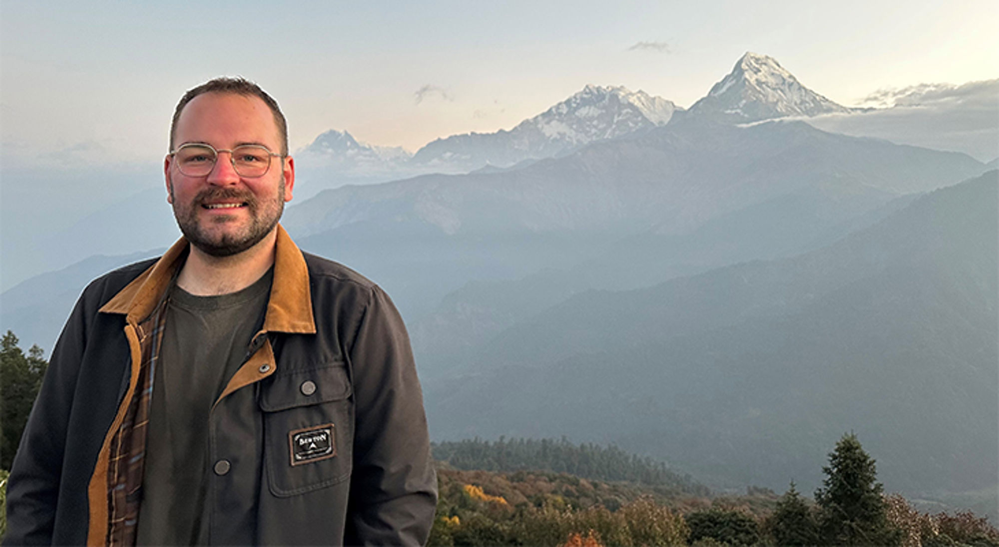 Ethan-Rory in Nepal Man poseert bij uitzichtpunt met besneeuwde bergtoppen op de achtergrond.