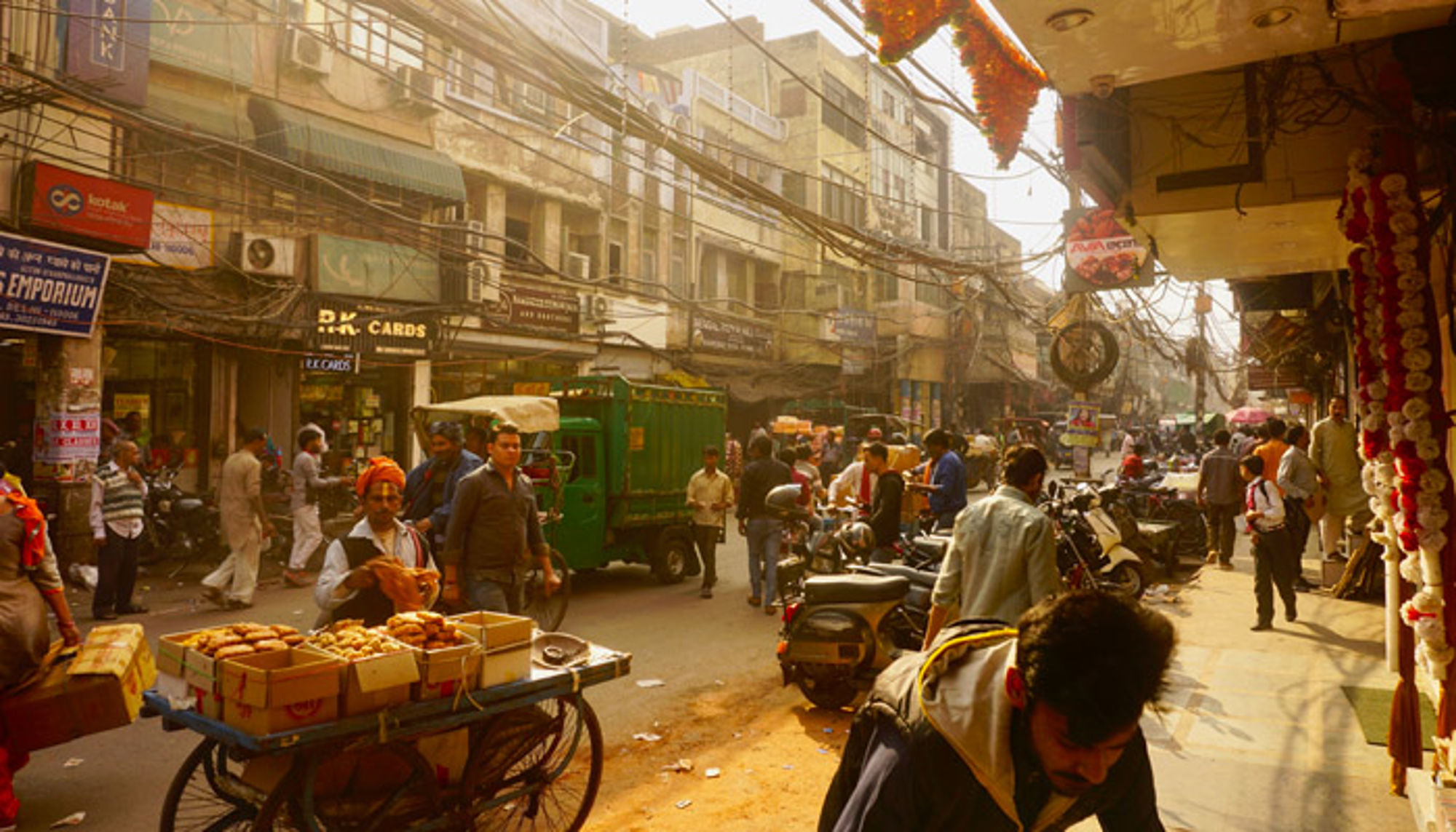 Een drukke straat in India Drukke straatmarkt in Delhi met kraampjes, scooters en voetgangers tussen winkels en bovenleidingen.