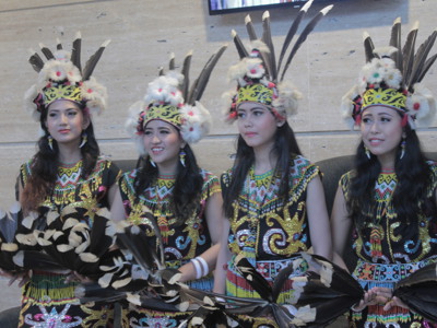 Vrouwen in kleurrijke traditionele dracht met verenhoofdtooi en danswaaier tijdens rondreis Kalimantan, Sulawesi & Molukken.