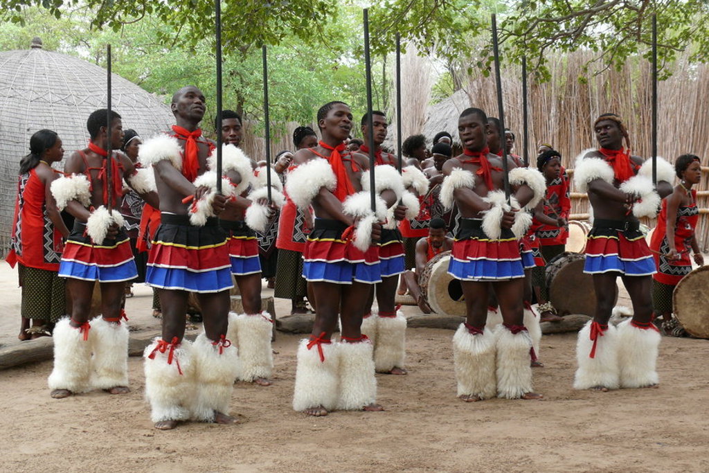 Traditionele dansgroep in eSwatini met kleurrijke kleding, speren en trommels tijdens een culturele voorstelling.