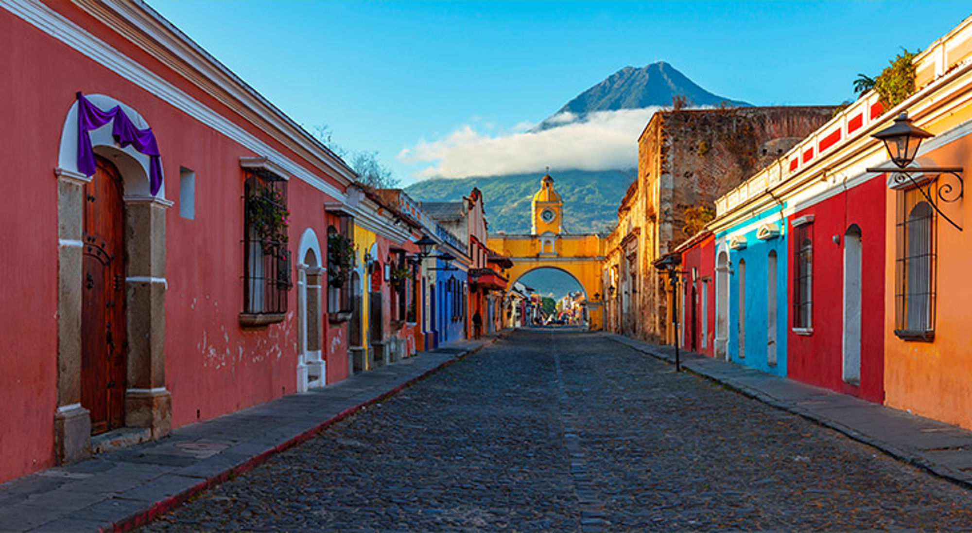 Reis buiten het hoogseizoen Kleurrijke straat in Antigua Guatemala met de Santa Catalina-boog en de vulkaan Agua op de achtergrond.