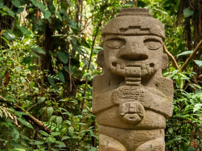 Stenen beeld in het archeologische park San Agustín, Colombia, omringd door tropisch groen.