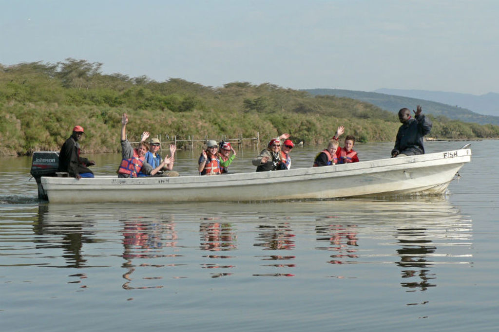 Groepsreizigers in reddingsvesten zwaaien vanaf een boot op een meer in Kenia tijdens de rondreis.