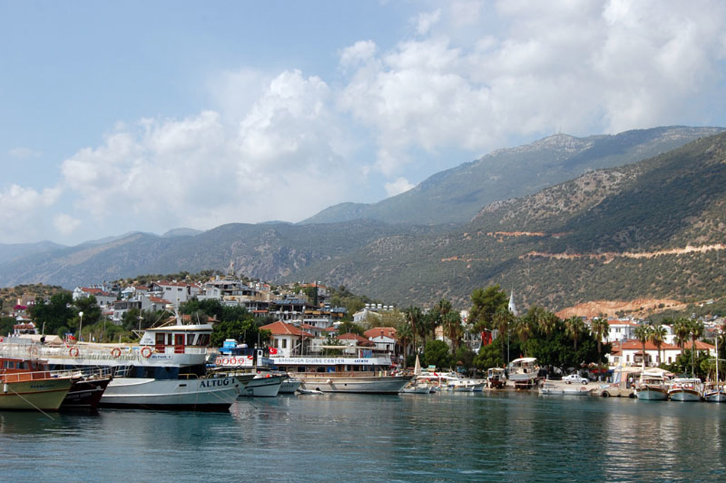 Haven in Zuid-Turkije met boten, witte huizen en bergen op de achtergrond.