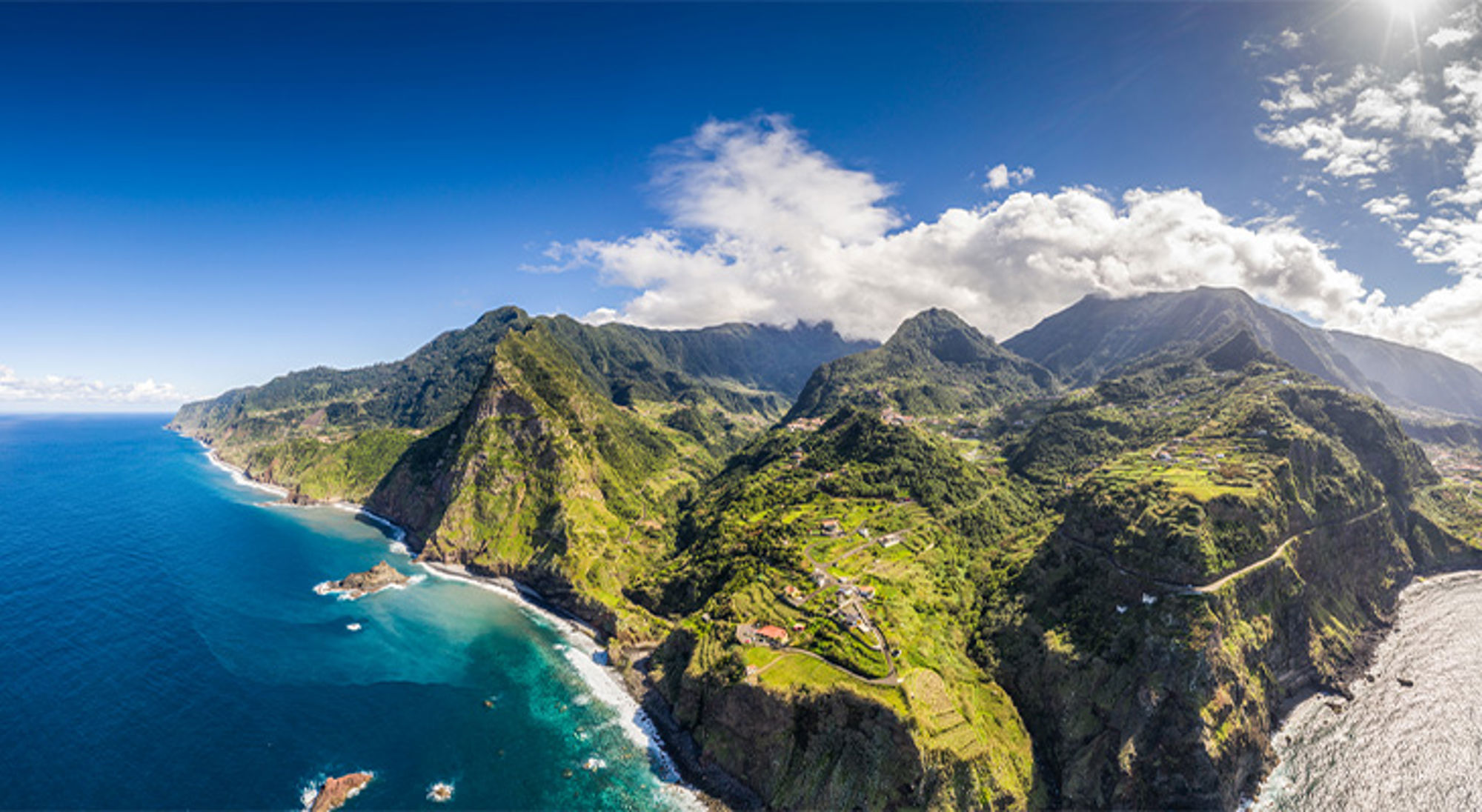 Madeira Panoramisch uitzicht op groene bergen en ruige kustlijn met turquoise zee onder een blauwe lucht.