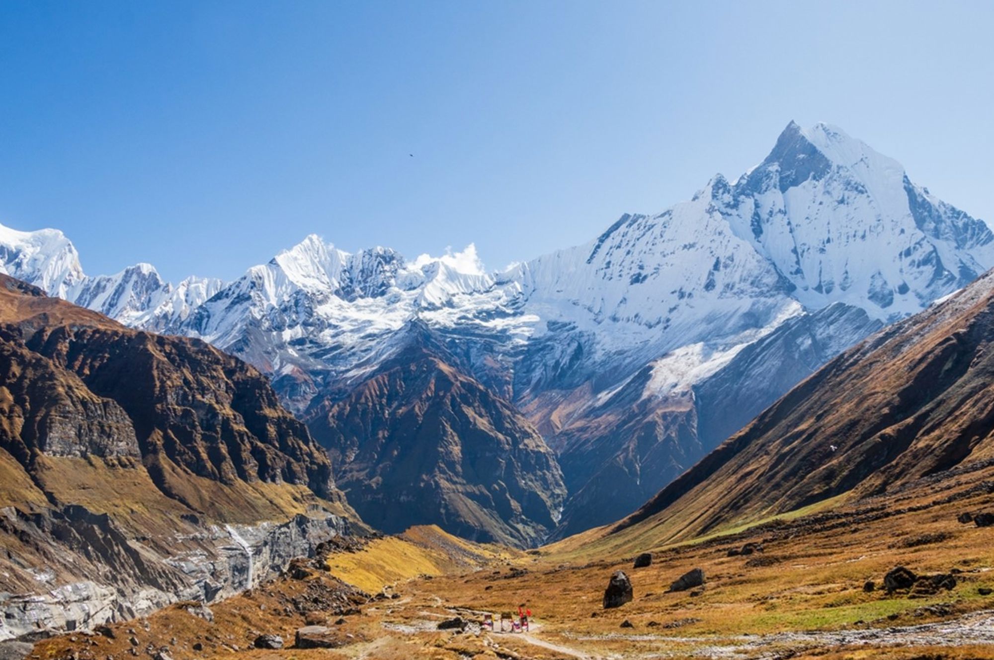 Sneeuwbedekte Himalaya-bergtoppen boven een brede vallei in Nepal, onder een heldere blauwe lucht.