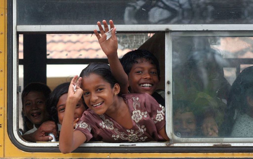 Vrolijke kinderen zwaaien uit het raam van een bus tijdens een groepsrondreis door Sri Lanka.