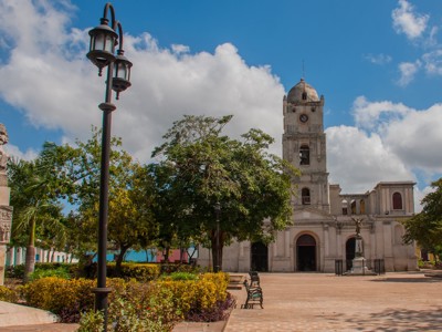Plein met kathedraal en klokkentoren in Cienfuegos, Cuba, onder een blauwe lucht met wolken.