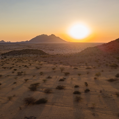 Zonsondergang boven de uitgestrekte woestijnvlakte in Namibië, met bergen aan de horizon.