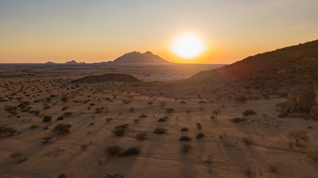 Zonsondergang boven de uitgestrekte woestijnvlakte in Namibië, met bergen aan de horizon.