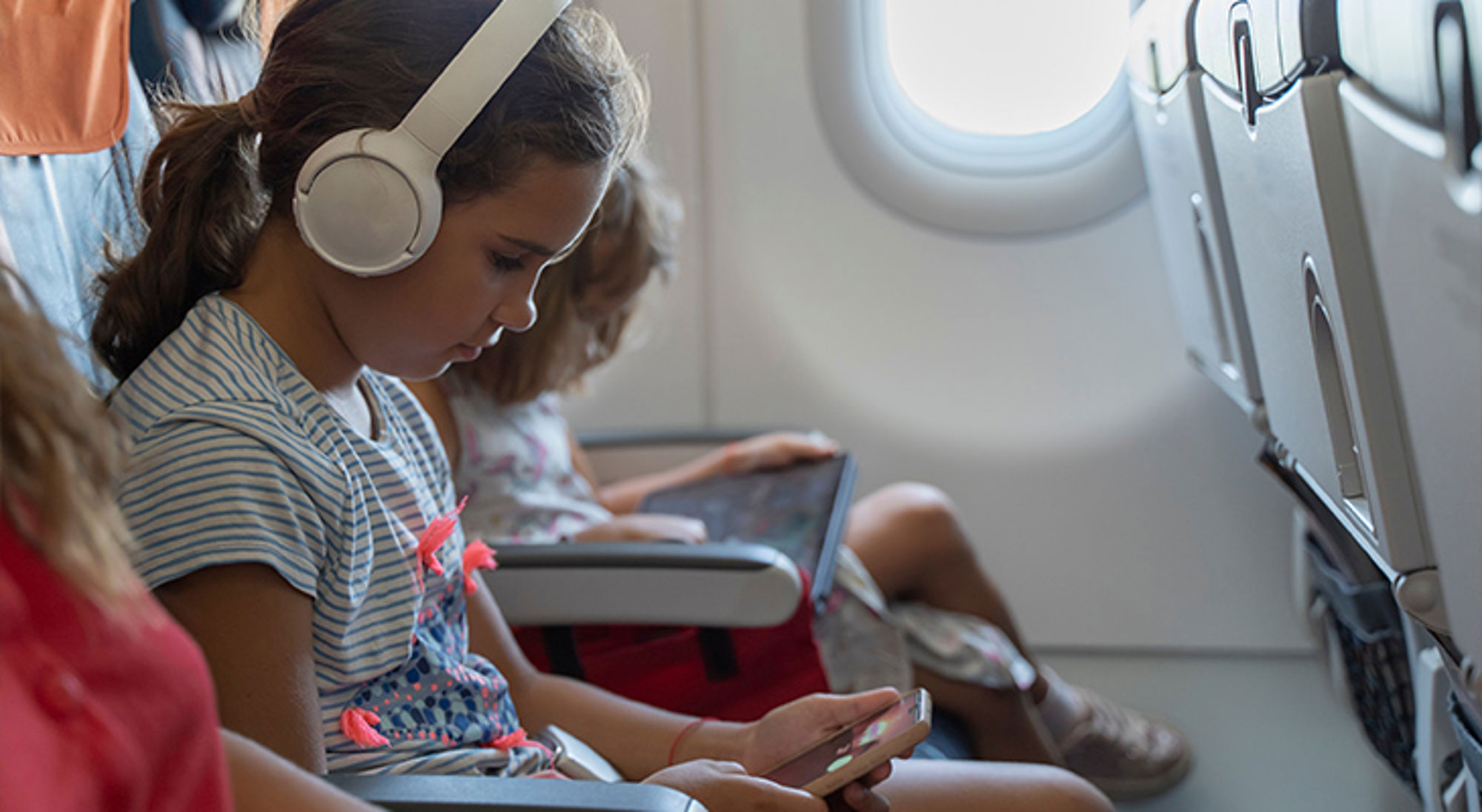 Koptelefoon vliegtuig Kinderen in een vliegtuigstoel met koptelefoon, smartphone en tablet tijdens de vlucht.