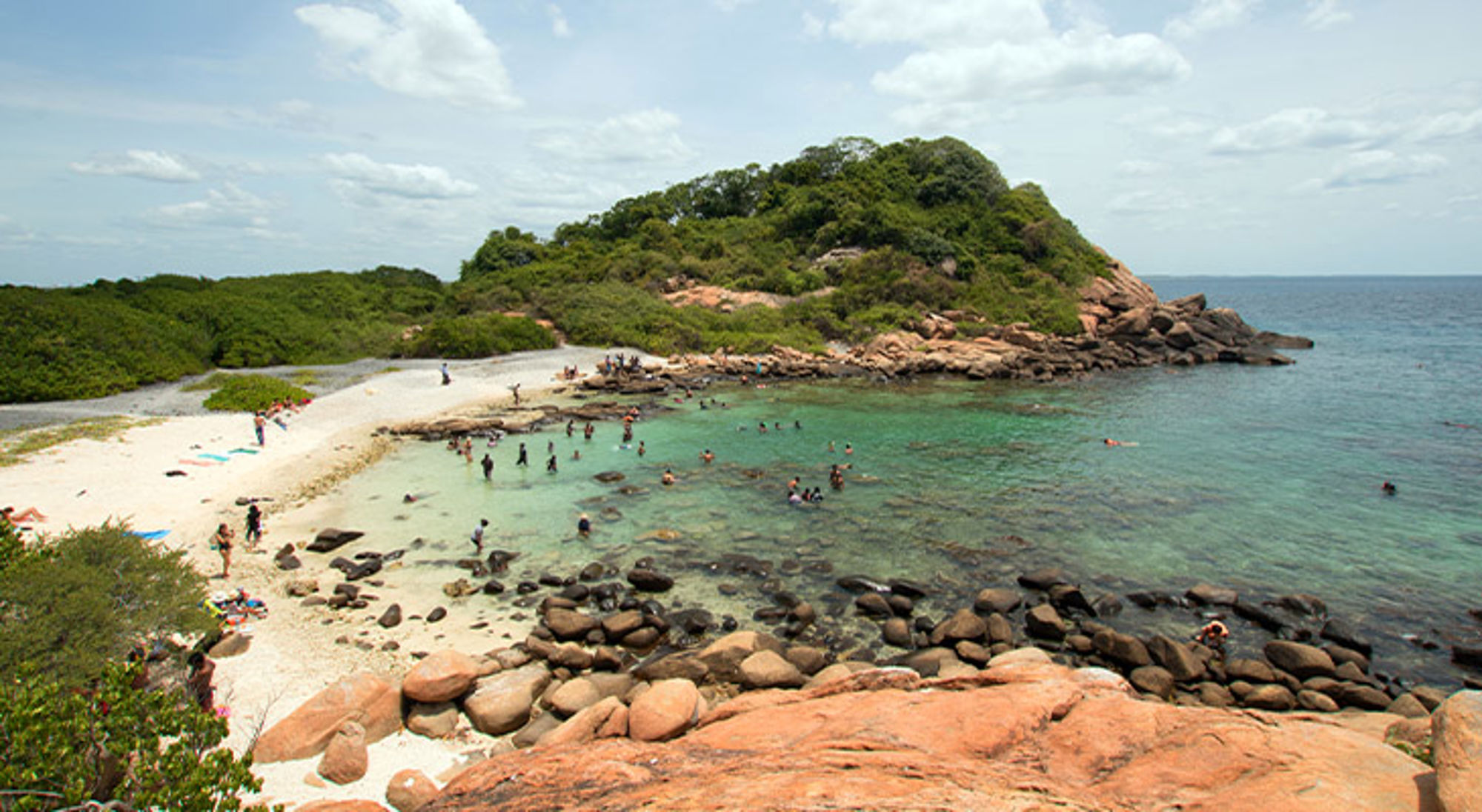 Pigeon Island Marine Park Baai met wit zandstrand, rotsen en helder zeewater waar mensen zwemmen en snorkelen.