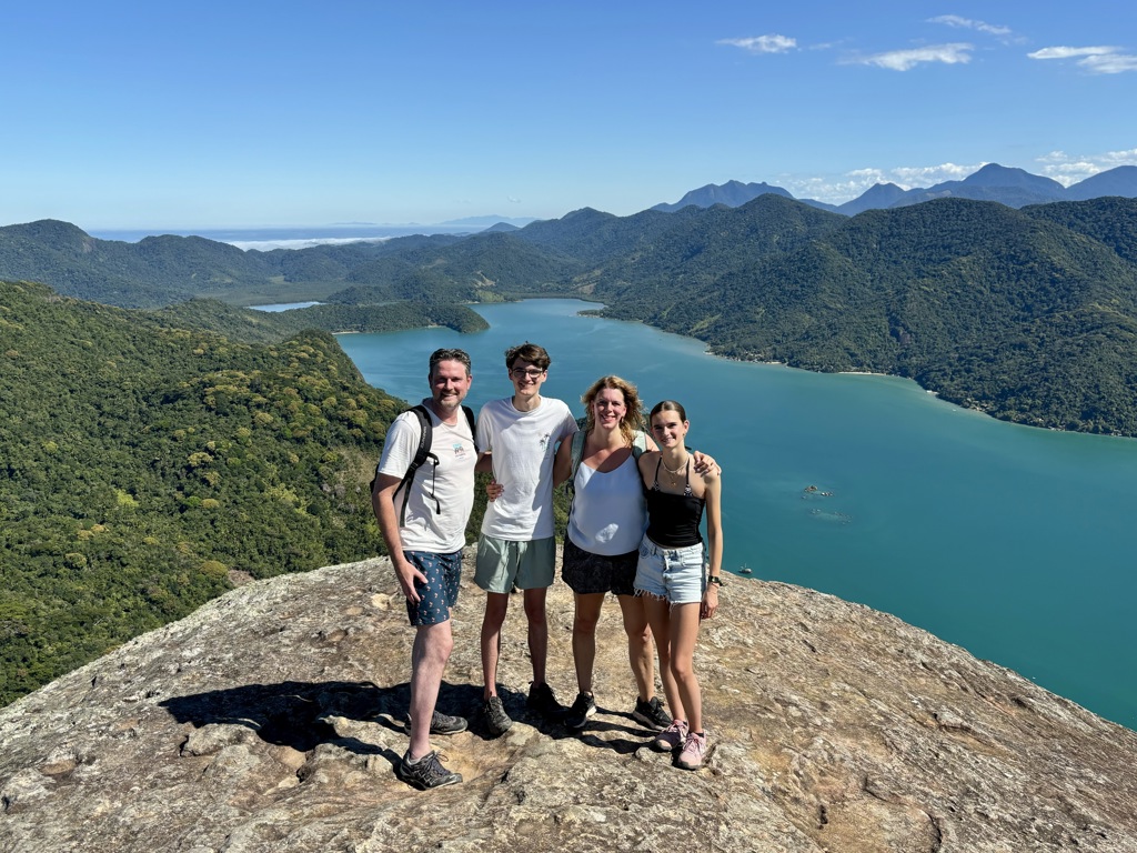 Gezin op een bergtop met uitzicht over een blauw meer en groene bergen tijdens familiereis Argentinië en Brazilië.