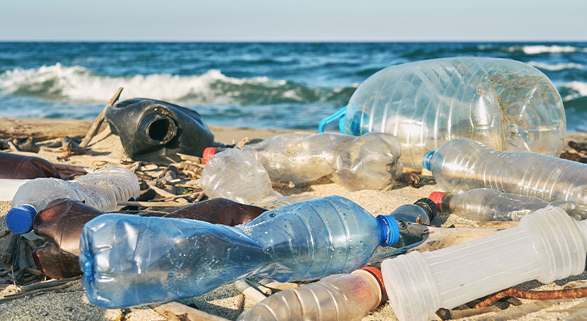 Plastic flessen en afval op het strand met de zee op de achtergrond.