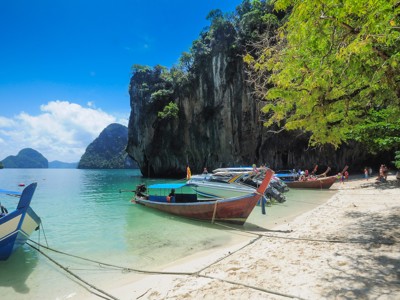 Longtailboten aan een wit zandstrand met kalksteenklif en helderblauw water in Zuid-Thailand.