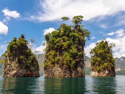 Karstrotsen begroeid met jungle in het helderblauwe water van Khao Sok Nationaal Park, Zuid-Thailand.