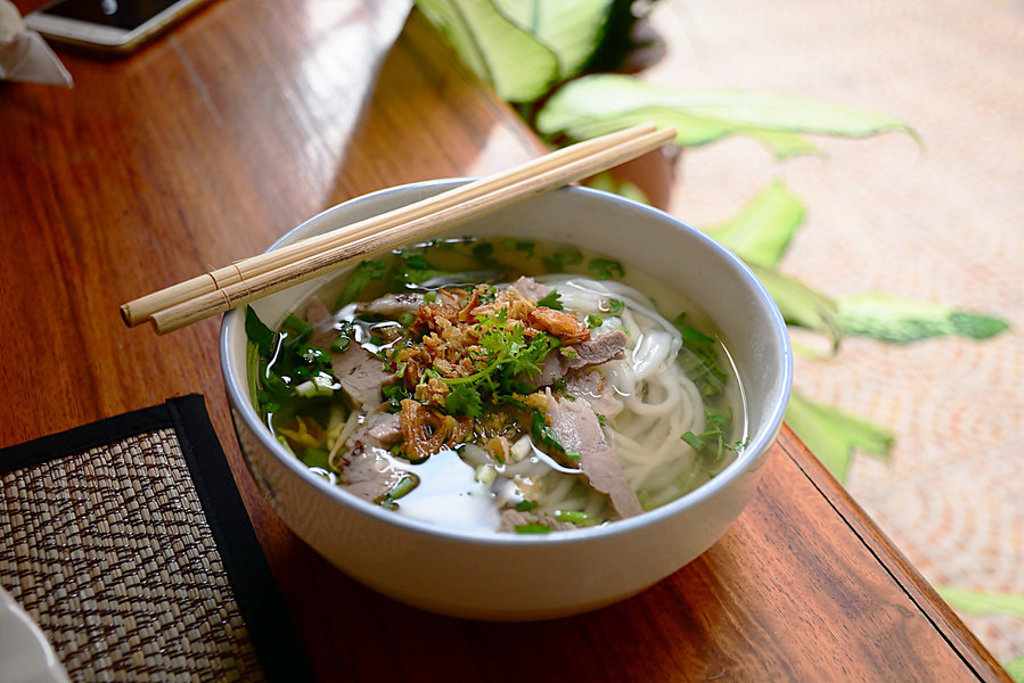 Kom Vietnamese pho-noedelsoep met kruiden en stokjes tijdens groepsrondreis Vietnam kort.