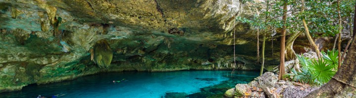 Helderblauw water in Cenote Dos Ojos, met rotswand en junglevegetatie rondom.