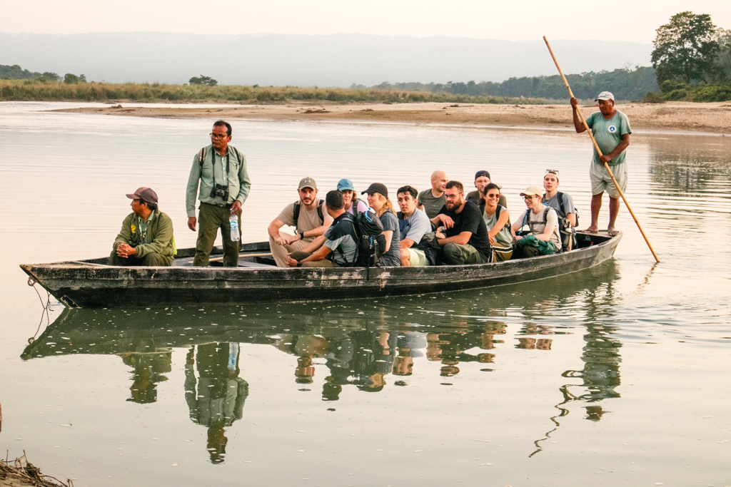 Groep reizigers steekt per houten boot een rivier over tijdens een 22-35ers reis Nepal.