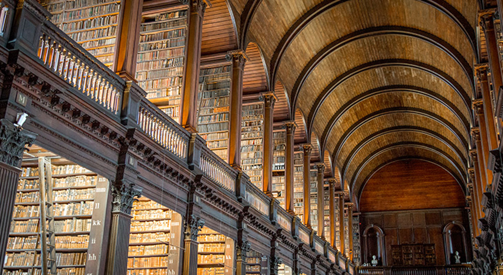 Trinity College bibliotheek, Dublin Interieur van een historische bibliotheek met hoge boekenkasten en een houten tongewelf.